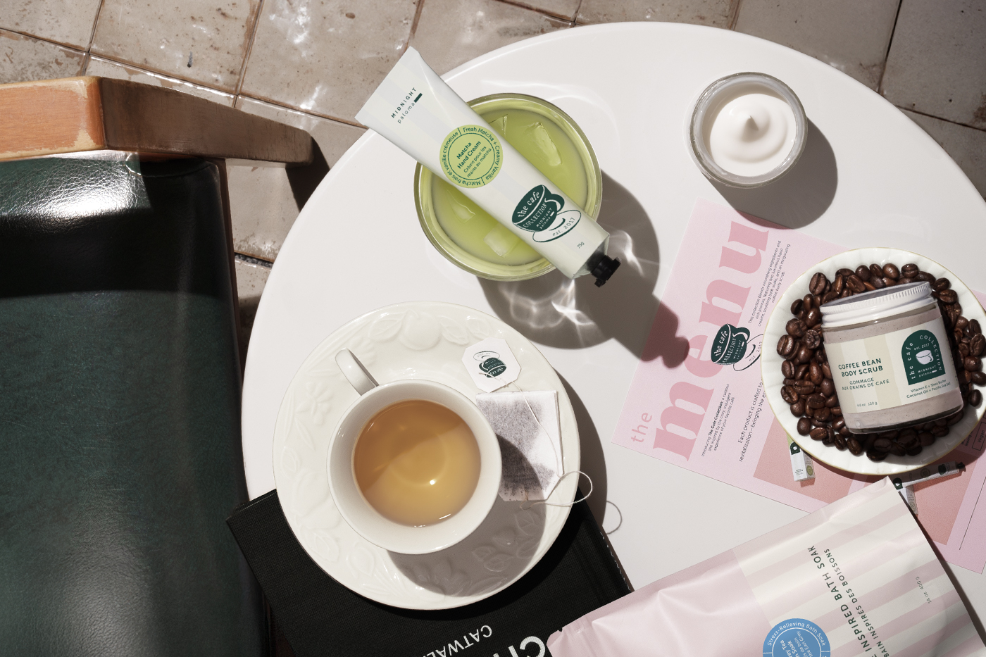 Danielle Gracioso Graphic Designer Vancouver BC Canada – Flat lay photo of the Café Collection by Midnight Paloma, featuring bath soak, hand cream, body scrub, and a tea cup on a round white table. Visual concept and photography by Danielle Gracioso.