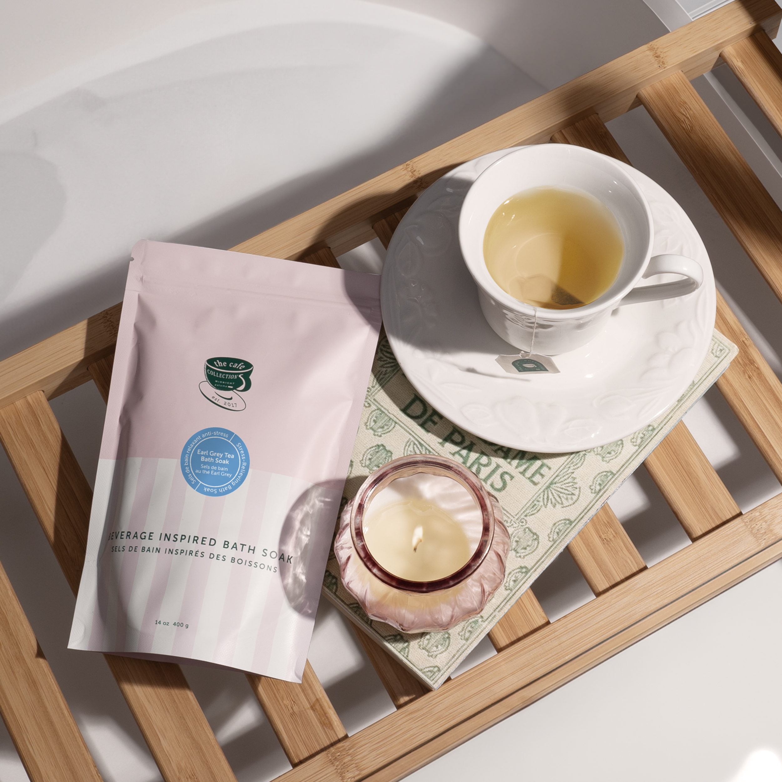 Danielle Gracioso Graphic Designer Vancouver BC Canada – Earl Grey Tea Bath Soak pouch styled on a wooden tub tray with a candle, book, and tea cup, creating a cozy spa vibe. Visual styling and photo by Danielle Gracioso.